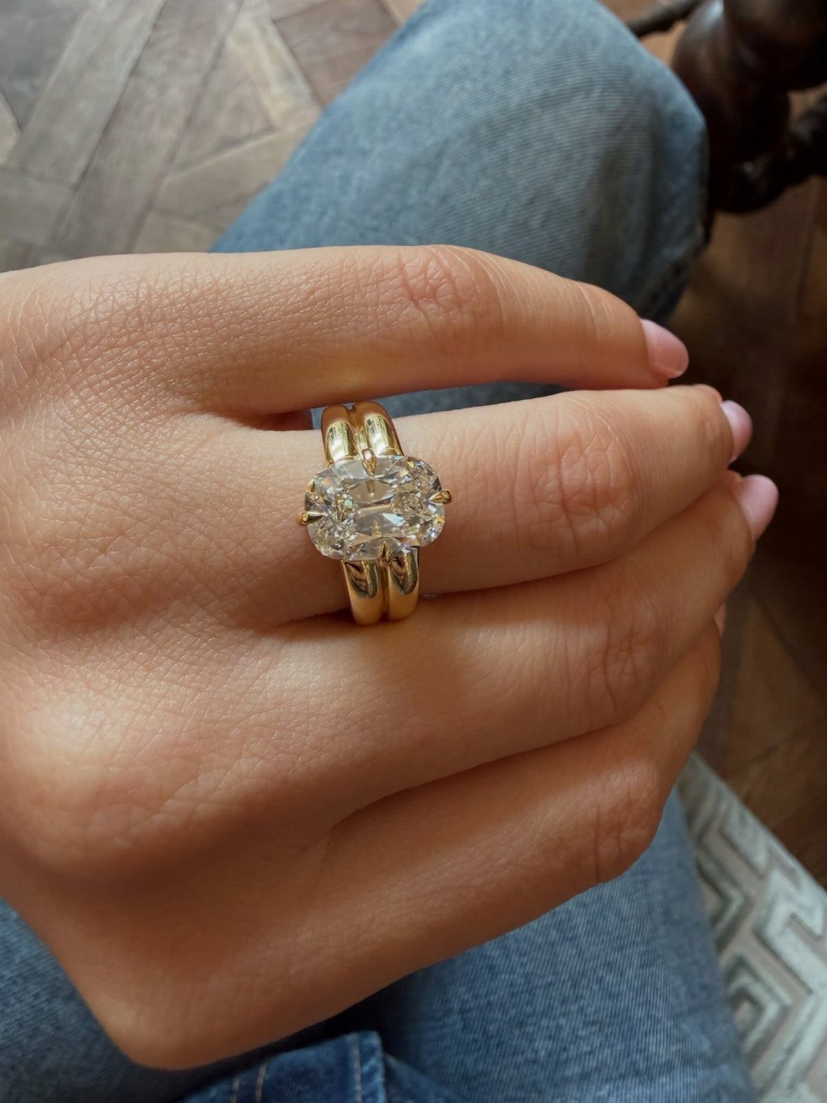 Two gold engagement rings with an oval diamond on a person's finger.