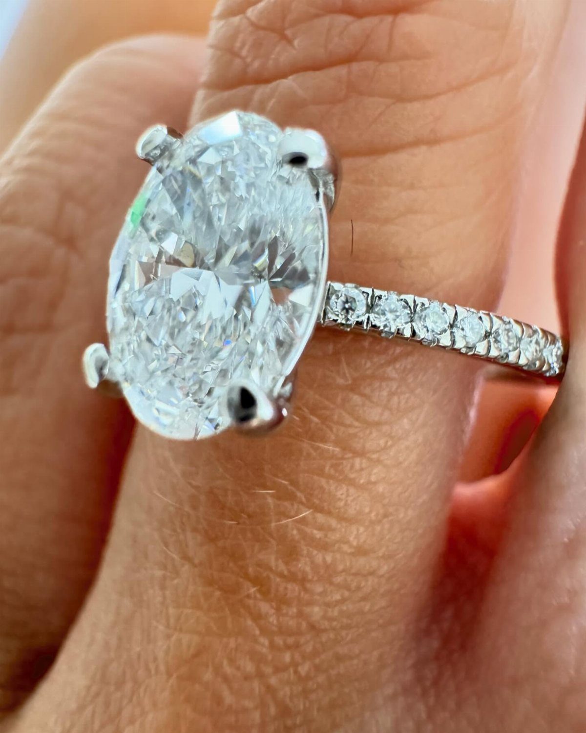 Oval-cut diamond engagement ring with a pavé band on a person's finger