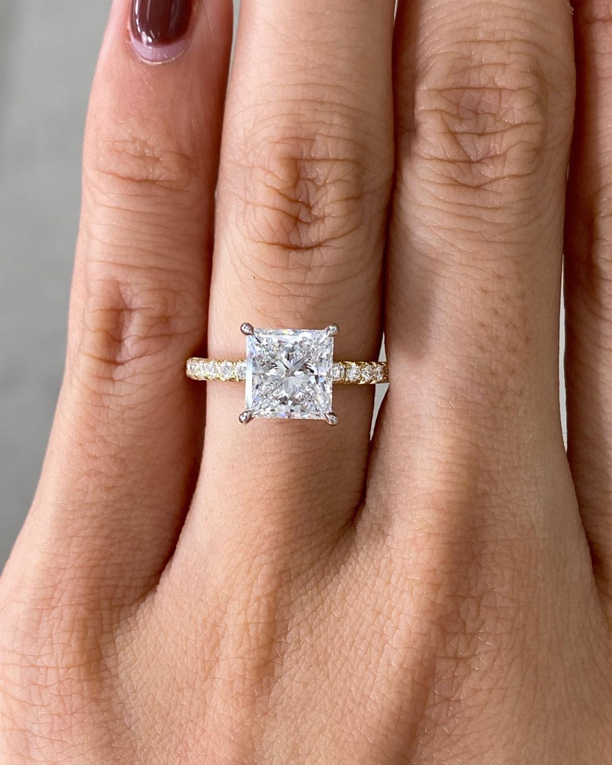 Princess cut diamond engagement ring with a gold pavé band on a finger