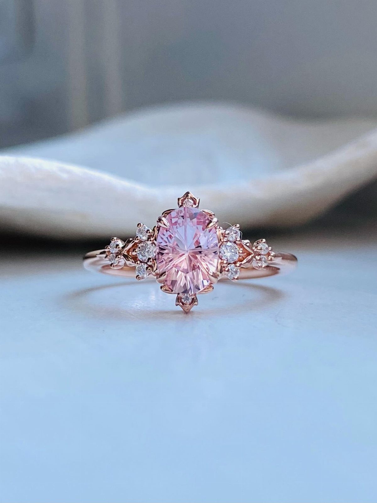 Rose gold engagement ring with oval pink gemstone and small side diamonds.