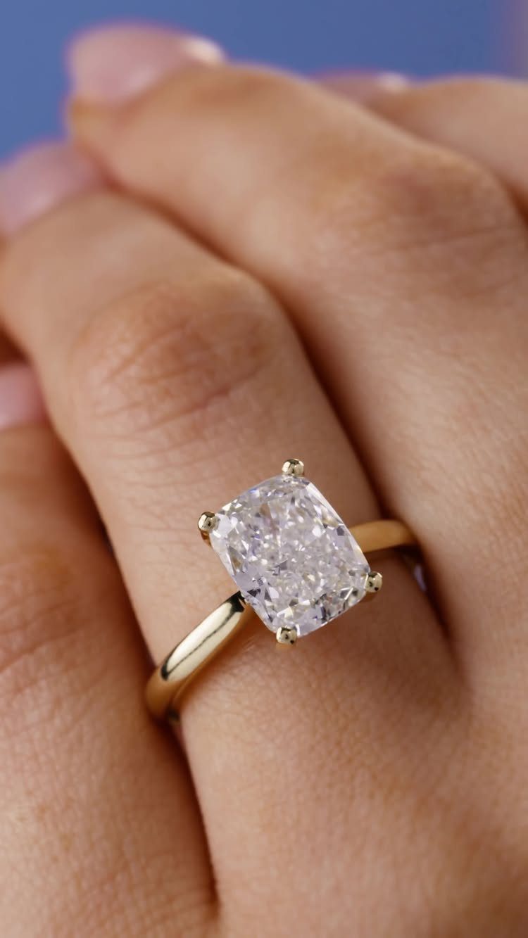 Gold engagement ring with a single cushion-cut diamond on a person's finger