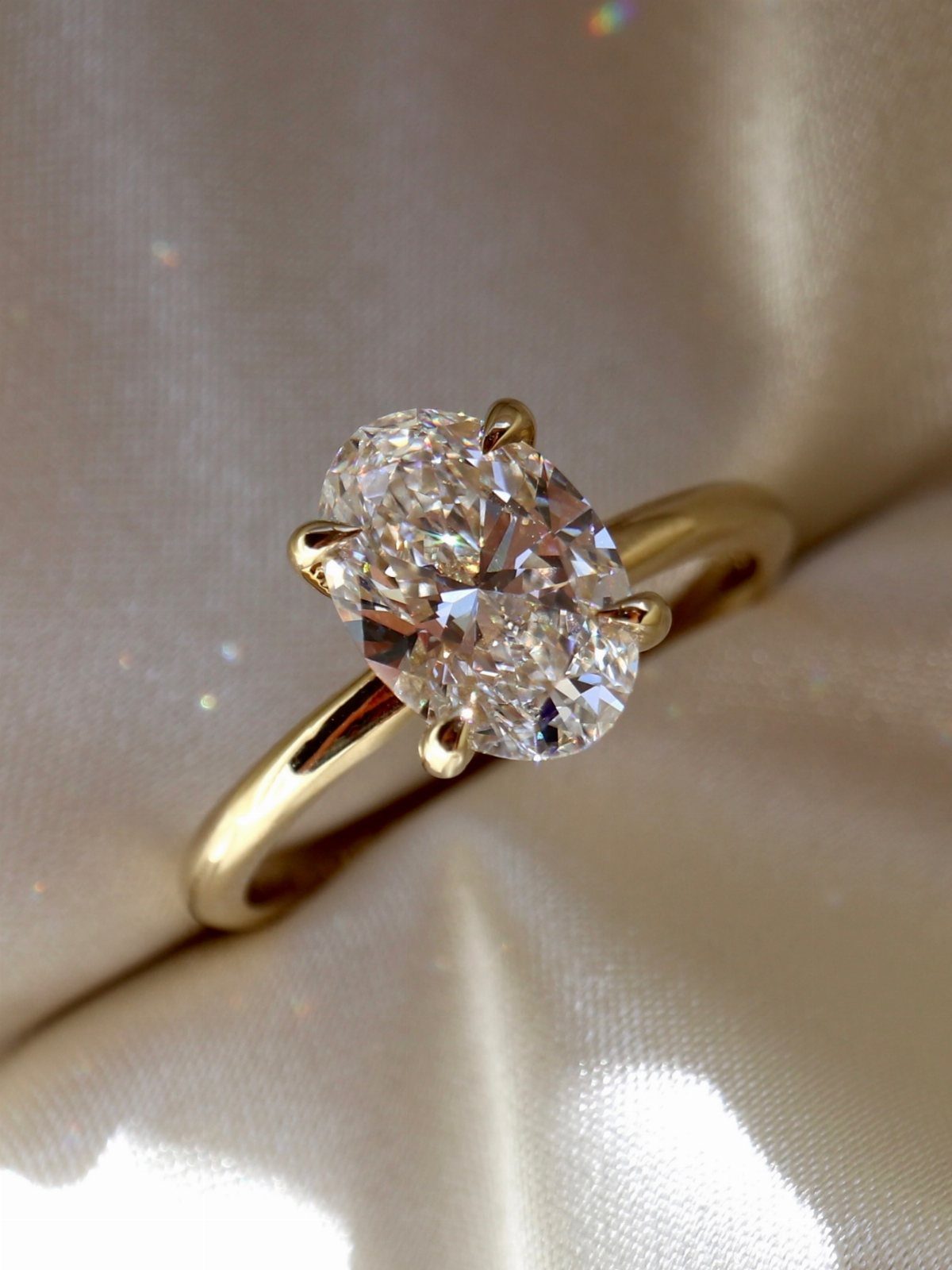 Gold engagement ring with an oval diamond resting on cream satin fabric