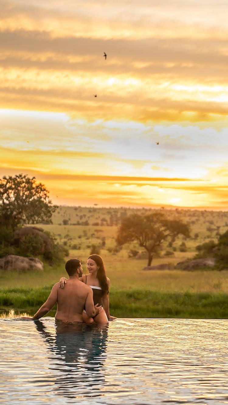 Couple embracing in an infinity pool overlooking a golden African savanna at sunset.