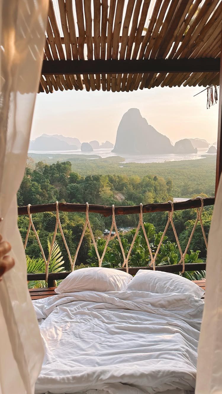 Bed with white linens in a bamboo hut overlooking tropical karst mountains.