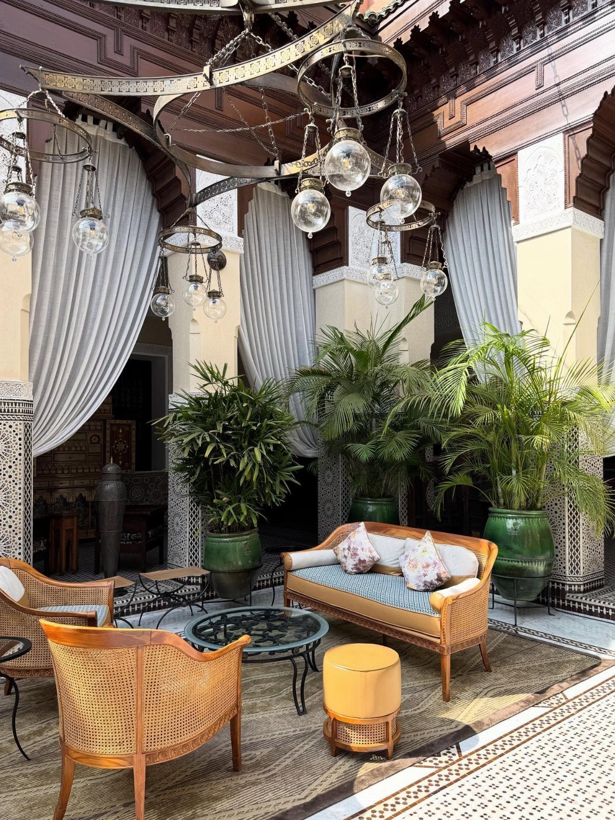 Ornate Moroccan courtyard with carved wood, glass lanterns, and wicker furniture with plants.