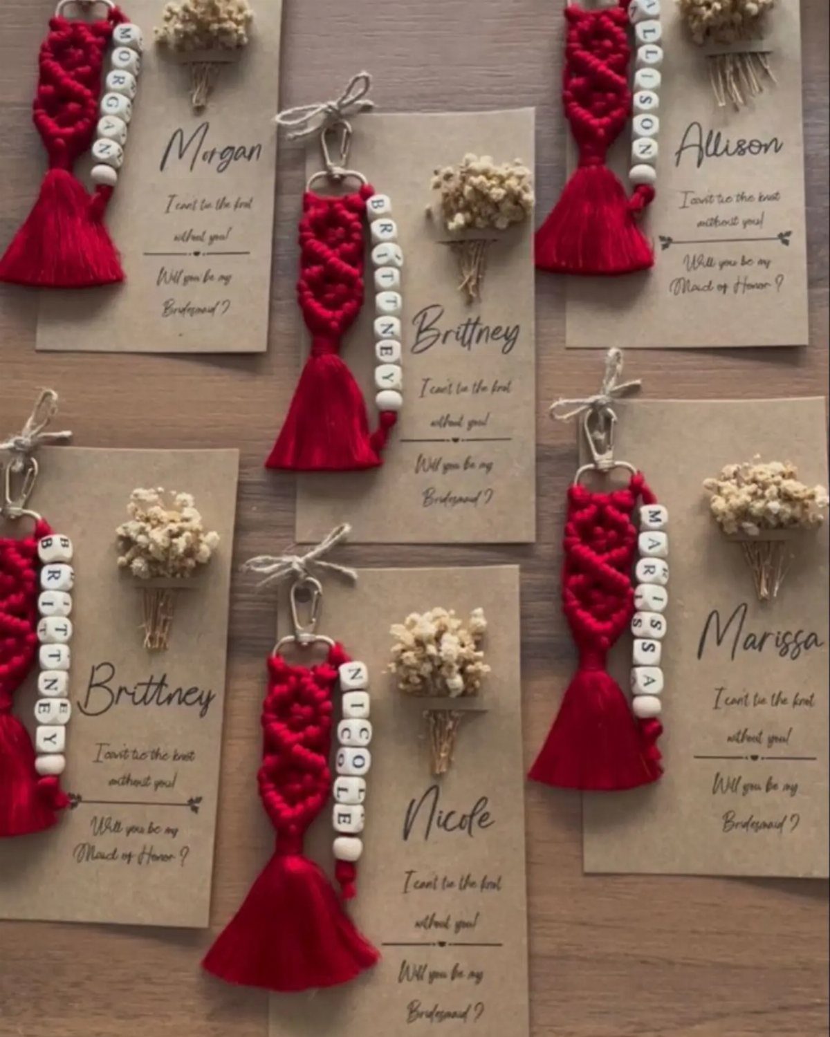 Red dress-shaped keychains with personalized names and small bouquets on proposal cards.