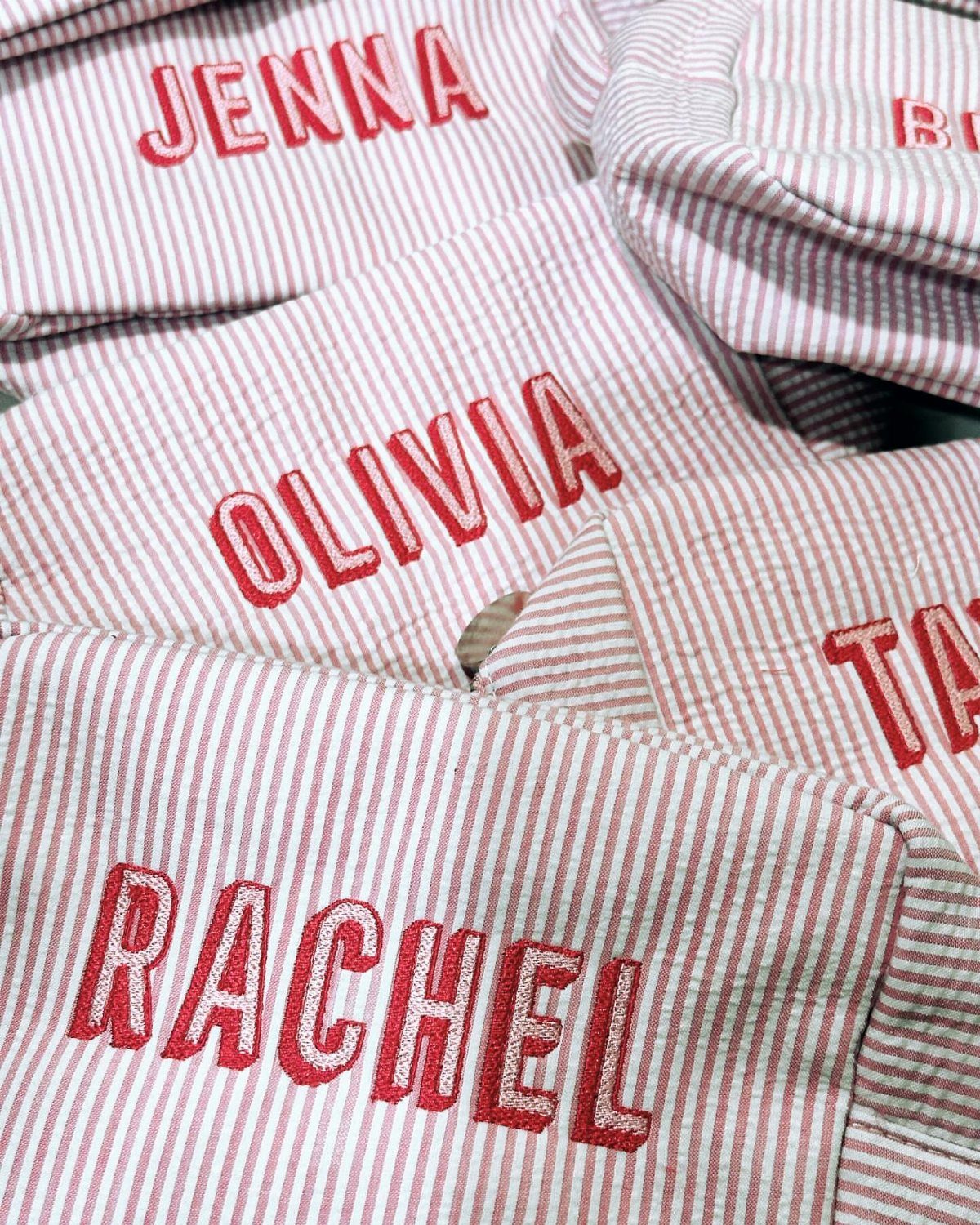 Red and white striped fabric makeup bags with personalized names embroidered in red.