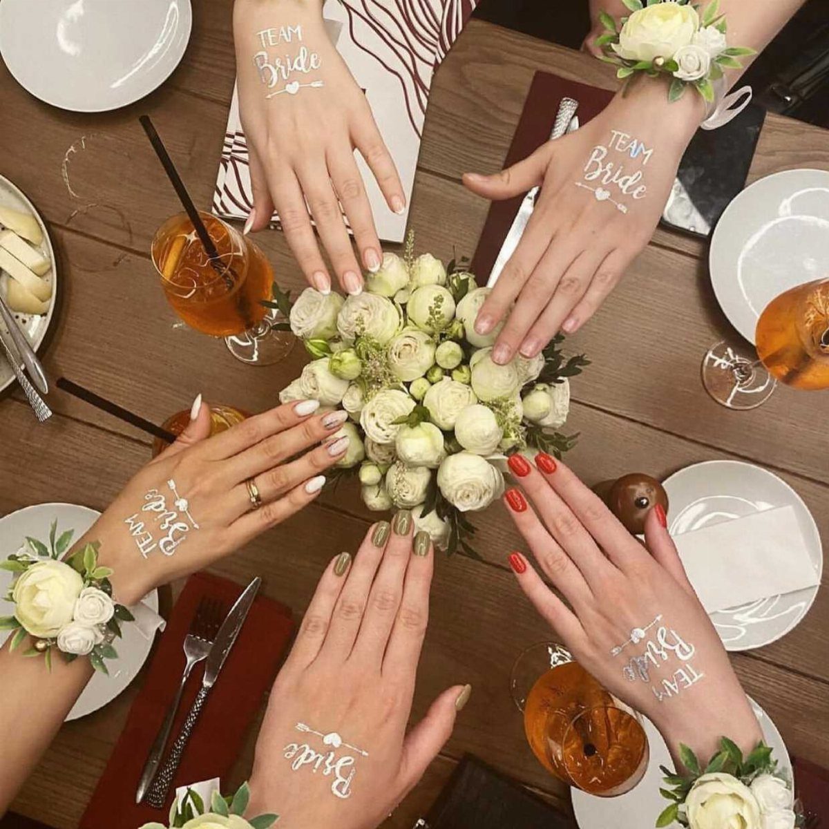 Women's wrists with white Team Bride temporary tattoos surrounding a white floral bouquet.