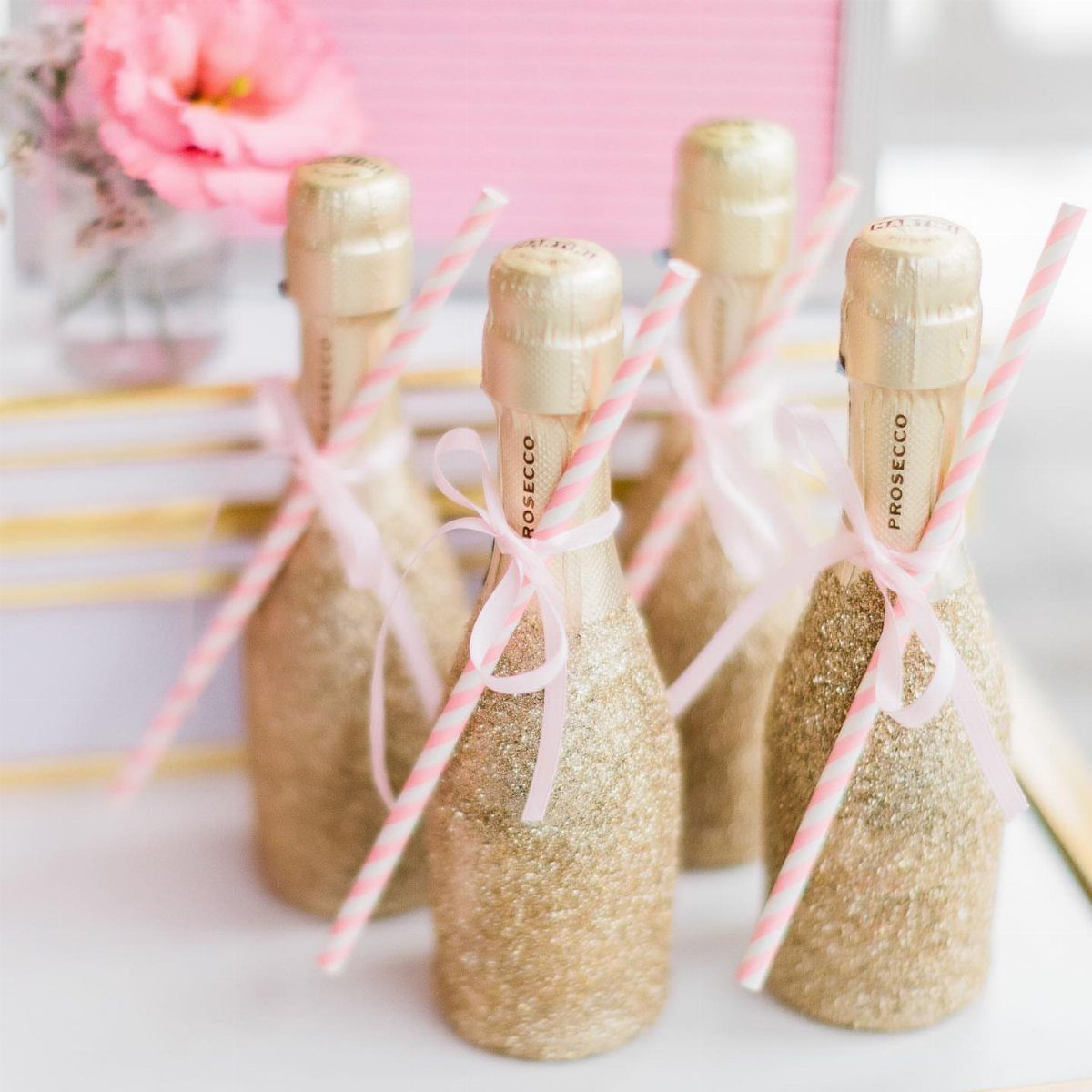 Mini Prosecco bottles covered in gold glitter with pink ribbons and striped straws.