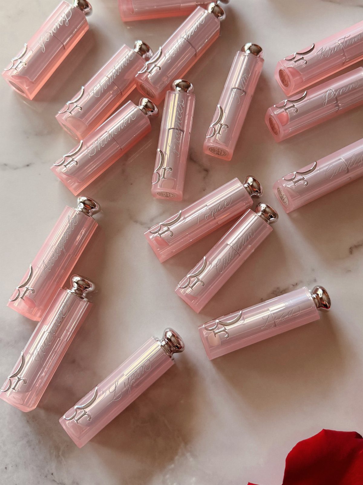 Pink personalized lip balm tubes with silver caps on a white marble surface.