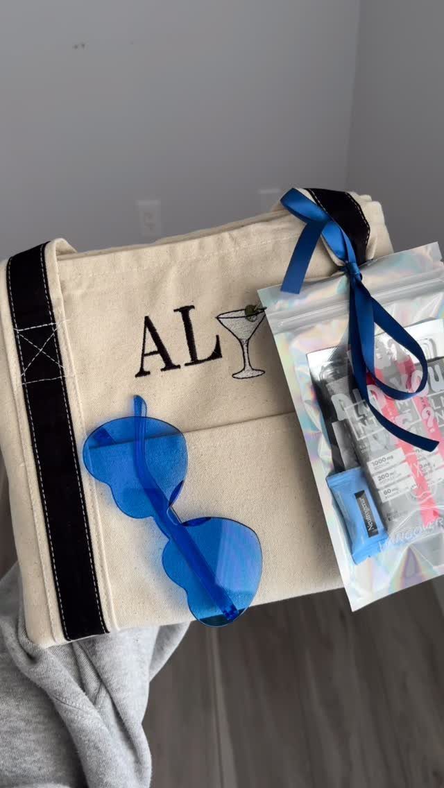 Beige canvas tote bag with blue heart sunglasses and a clear favor pouch.