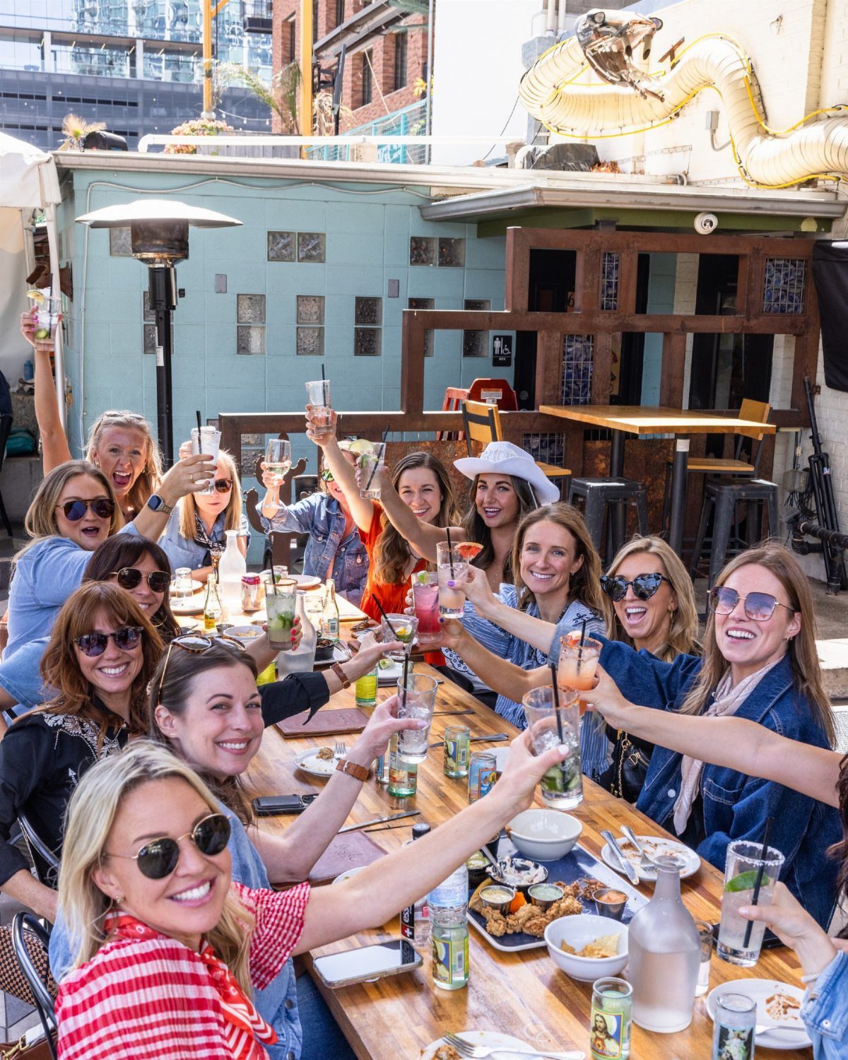 Group of women cheering with colorful cocktails at an outdoor brunch table.