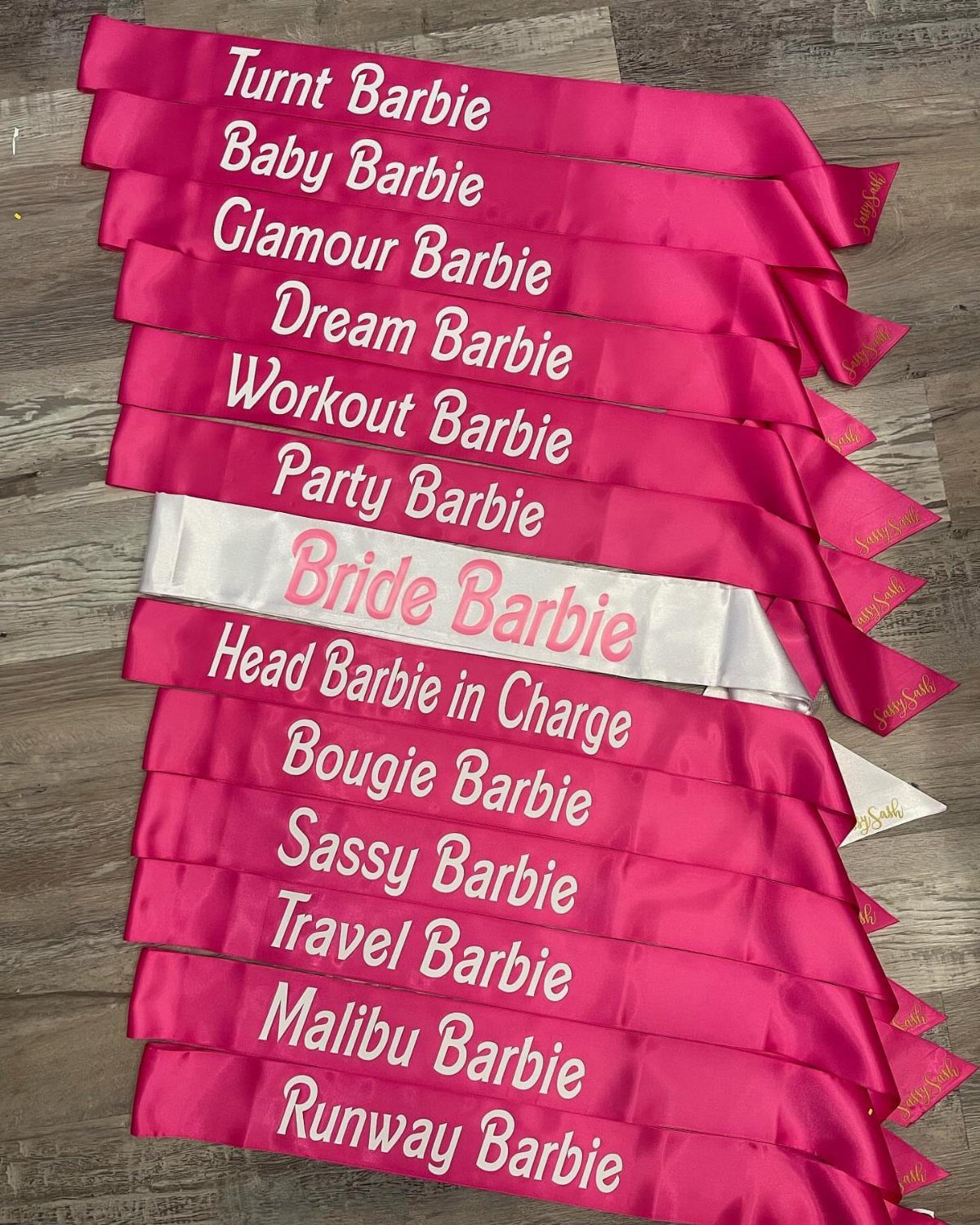 Pink and white satin sashes with Barbie themed text on a grey floor