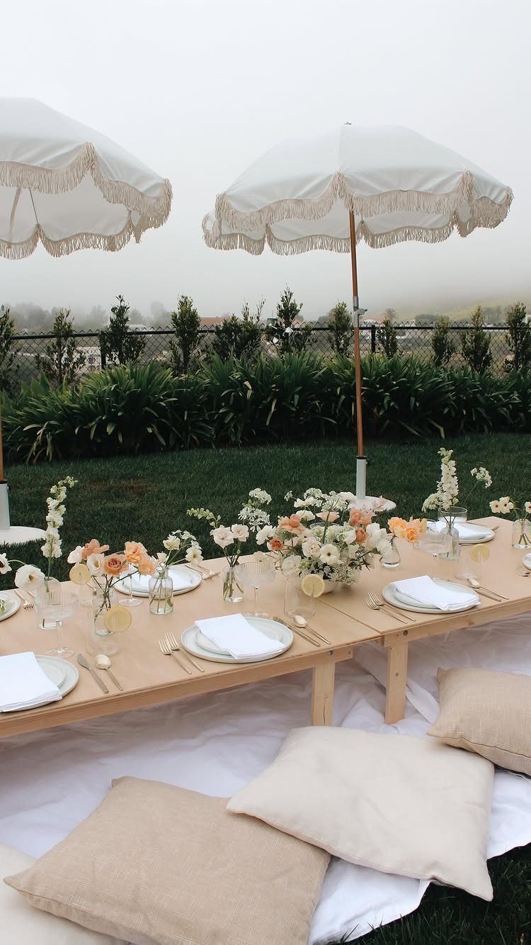 Low wooden picnic table with floral arrangements and white umbrellas on a lawn