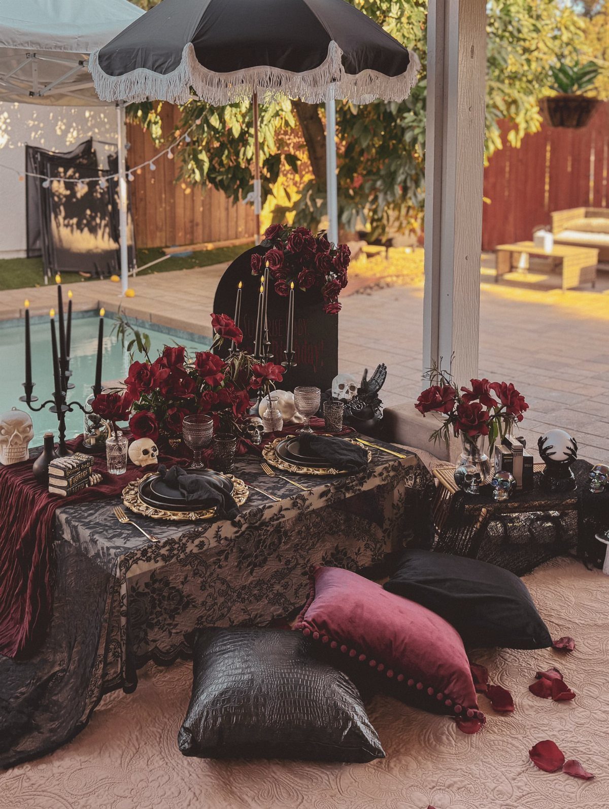 Darkly decorated outdoor table with red roses, black candles, and burgundy pillows.