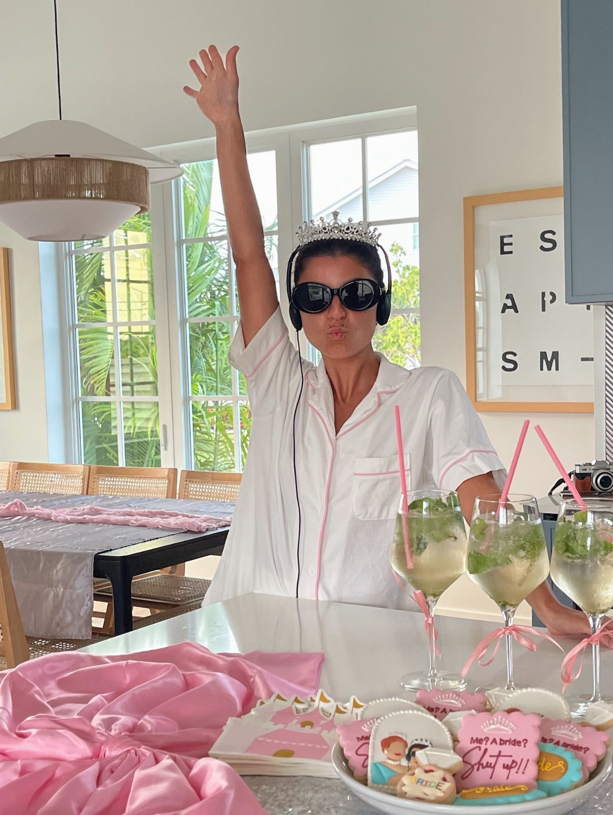 Woman in white pajamas and a tiara posing with themed cocktails and cookies.