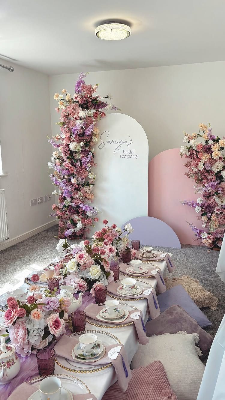 Tea party table setting with pink and purple flowers and arched backdrops.