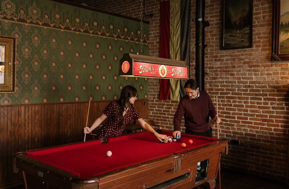 Couple playing pool in a vintage bar with red felt and brick walls
