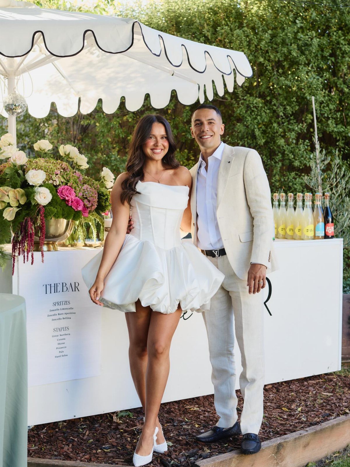 Couple in white formal attire posing in front of an outdoor white bar