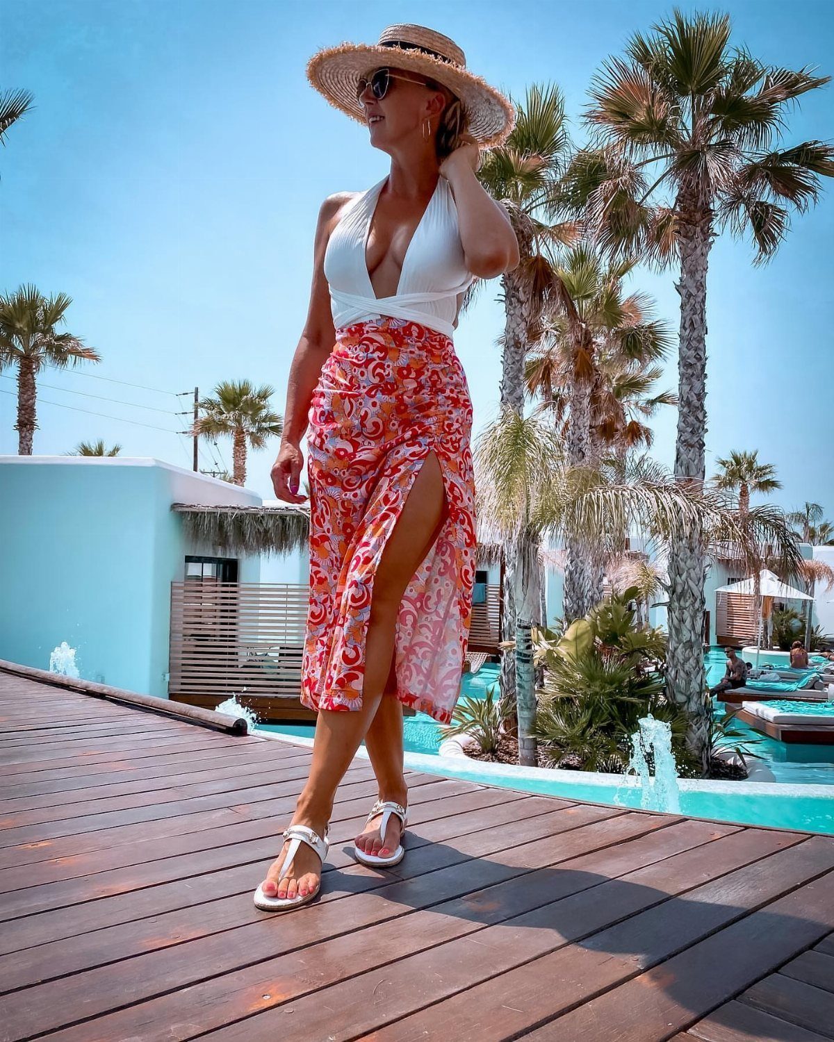 Woman in floral skirt and white top walking on wooden deck by pool