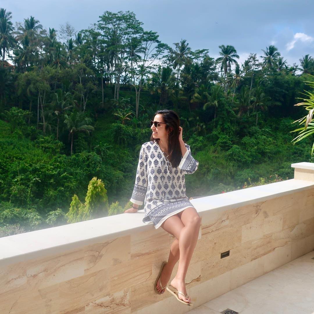 Woman in a blue and white patterned tunic dress sitting on a stone ledge.