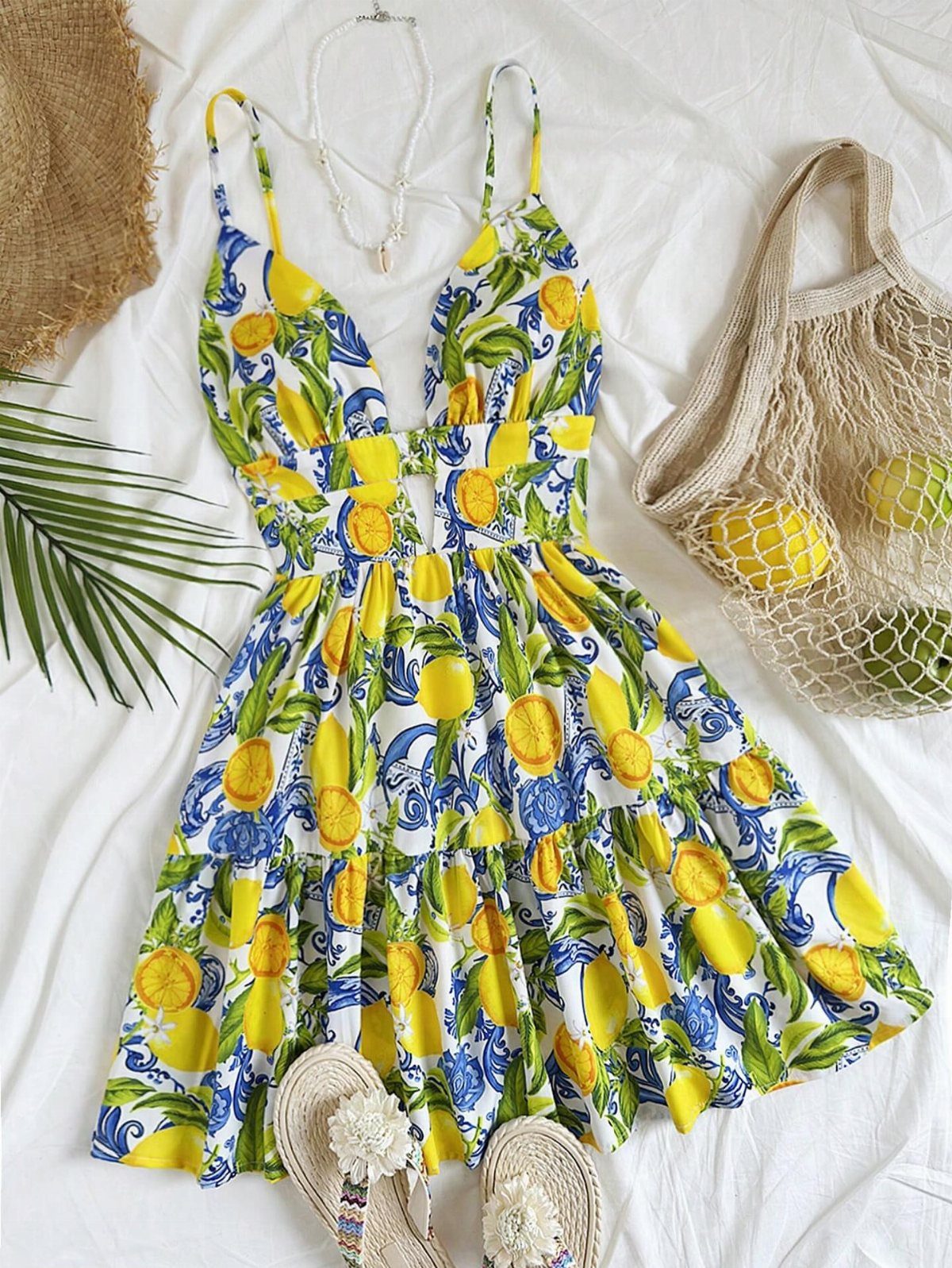 Lemon print sundress laid flat with sandals, a mesh bag, and a necklace.
