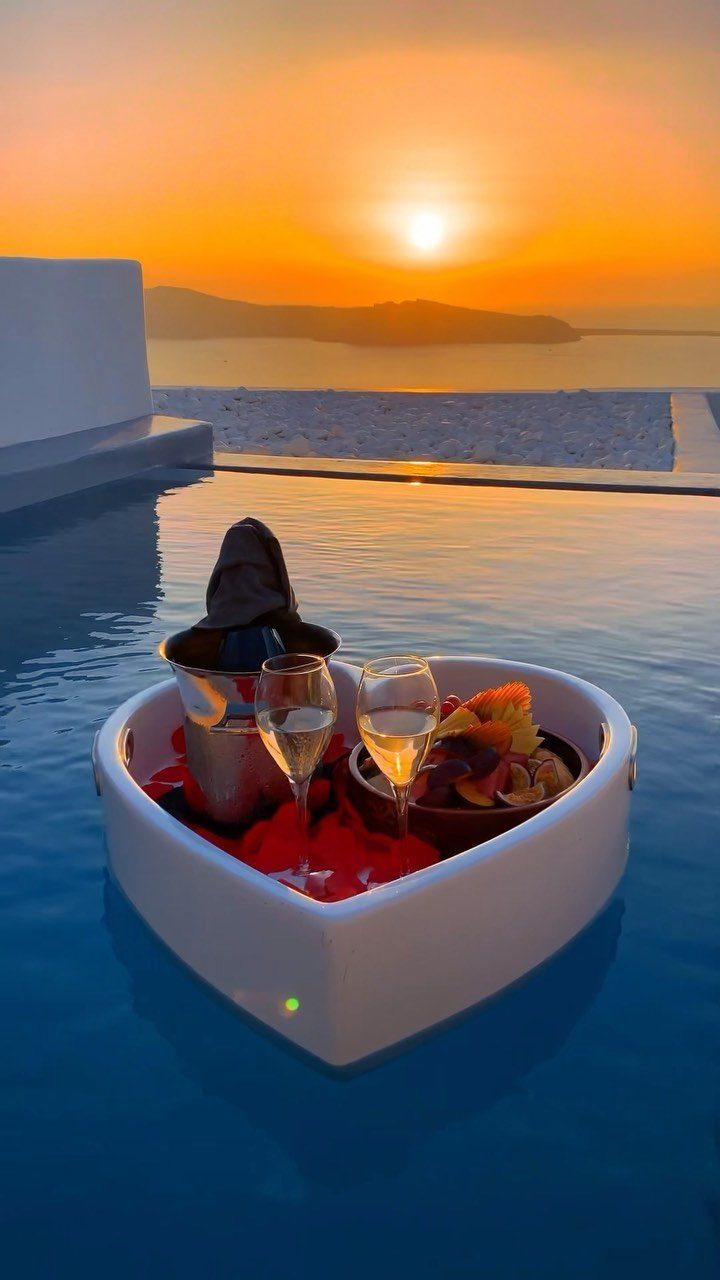 Heart-shaped floating breakfast tray with wine in an infinity pool at sunset