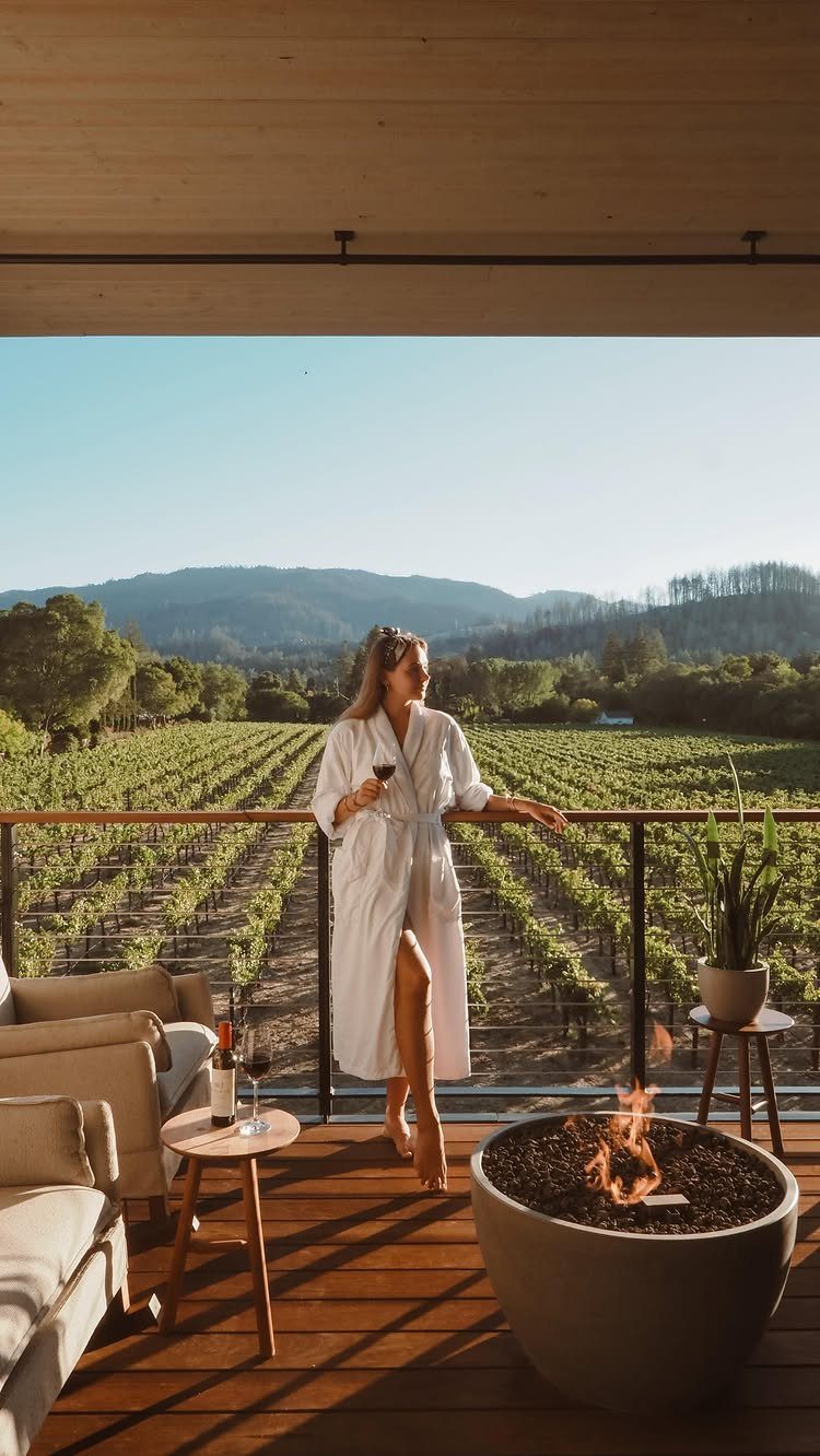 Woman in white robe overlooking a scenic vineyard from a luxury wooden deck