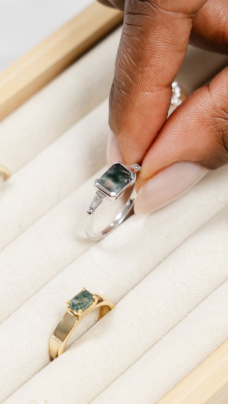 Silver and gold rings with square green gemstones in a white display box