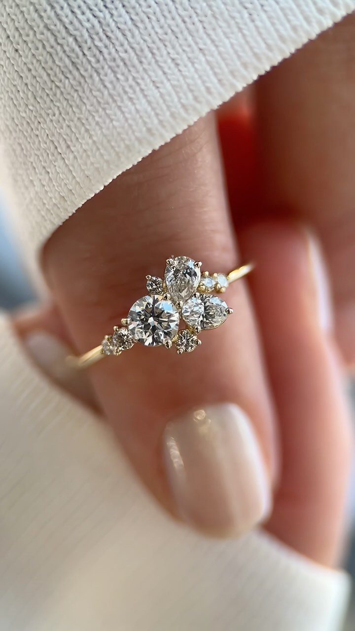Gold engagement ring with a cluster of diamonds on a finger with neutral nails