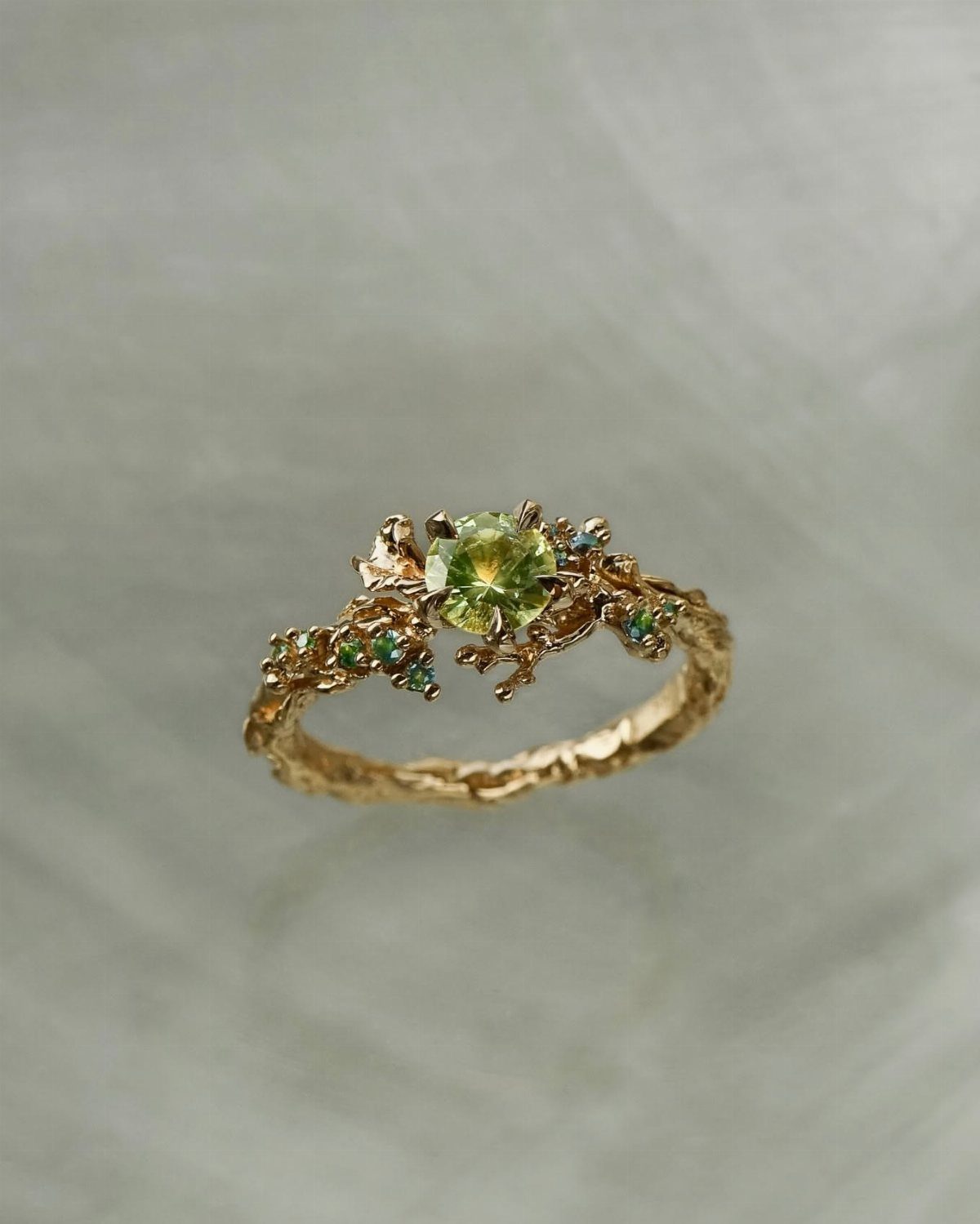 Gold ring with a green gemstone and organic leaf-like handcrafted details.