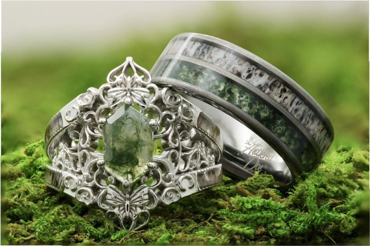 Ornate silver engagement ring with hexagonal green stone and matching inlay band on moss