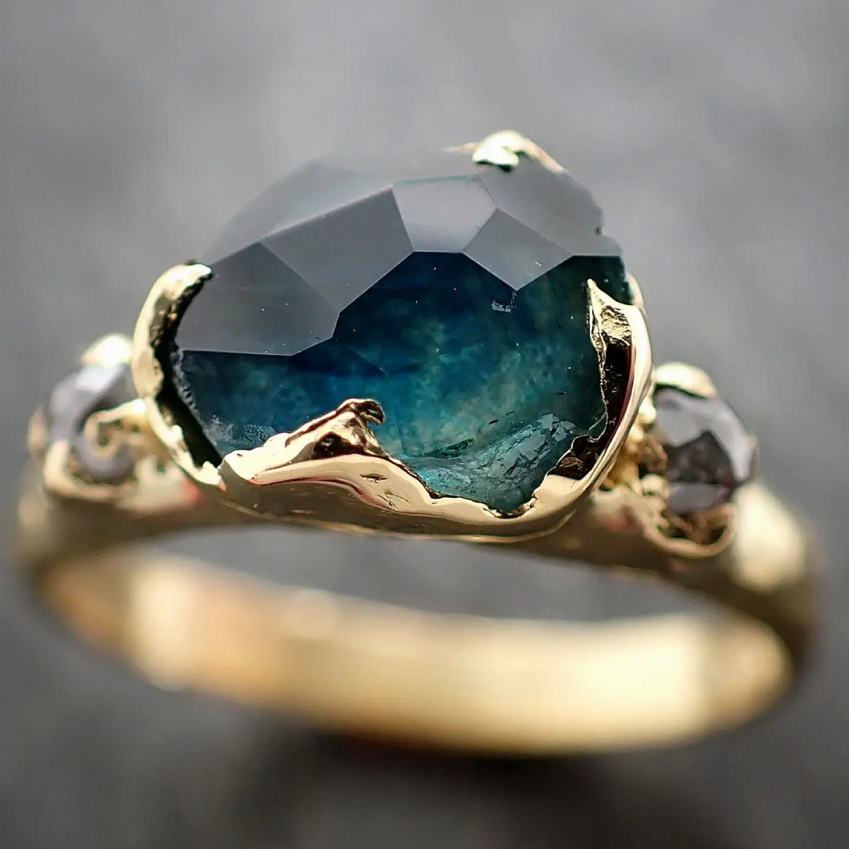 Gold ring with a faceted teal gemstone in an organic, curved setting.