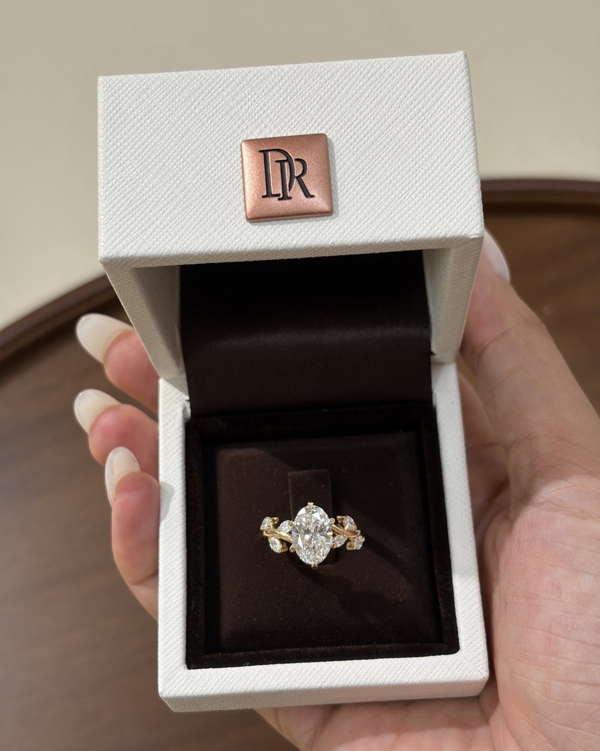 Gold engagement ring with oval diamond in a white jewelry box held by hand