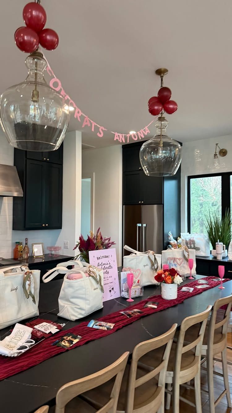 Party table setup with red runner, white gift bags, and pink drinks in kitchen