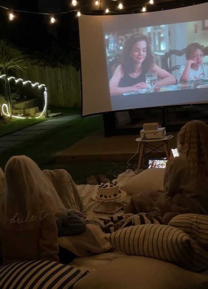 Two women watching a movie on a projector screen in a cozy backyard
