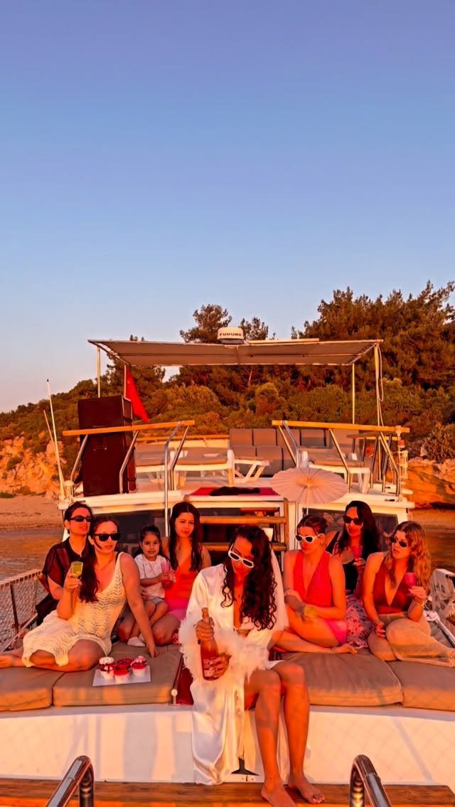 Group of women celebrating on a boat deck near a wooded coastline.