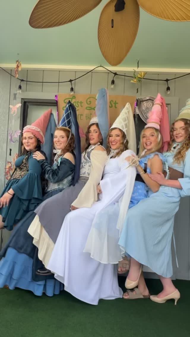 Six women in medieval gowns and conical hats posing for a group photo.