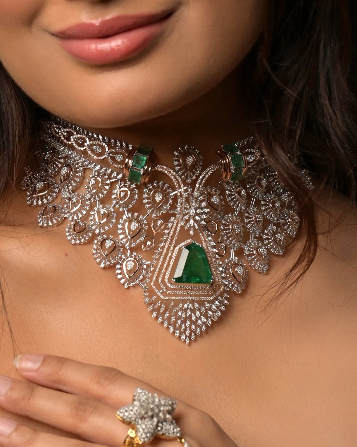 Ornate diamond necklace with green emeralds and a star-shaped diamond ring on a woman