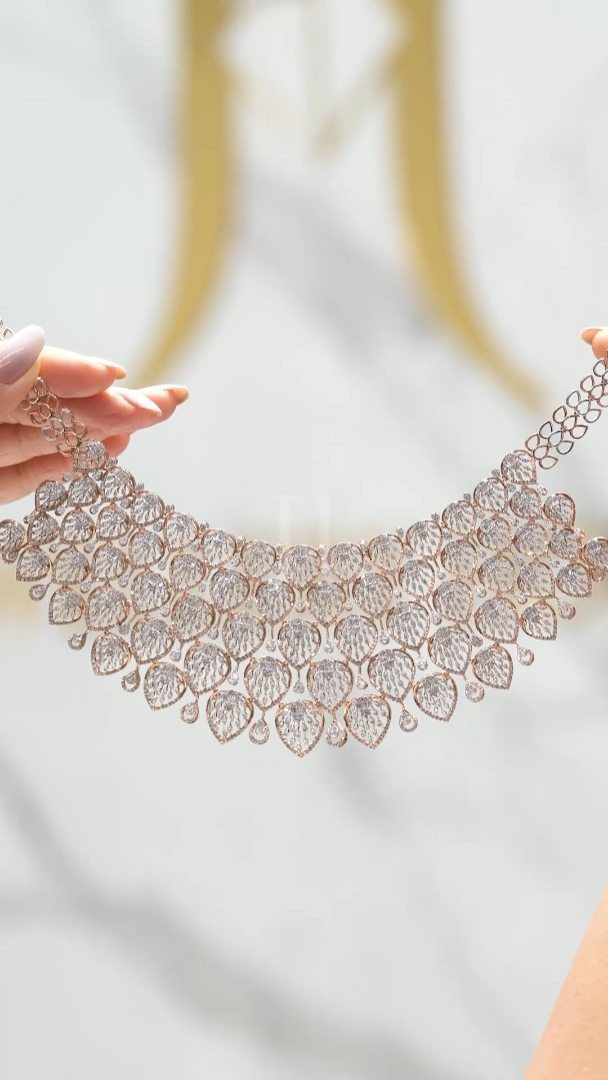 Ornate gold and diamond collar necklace held up by two hands.