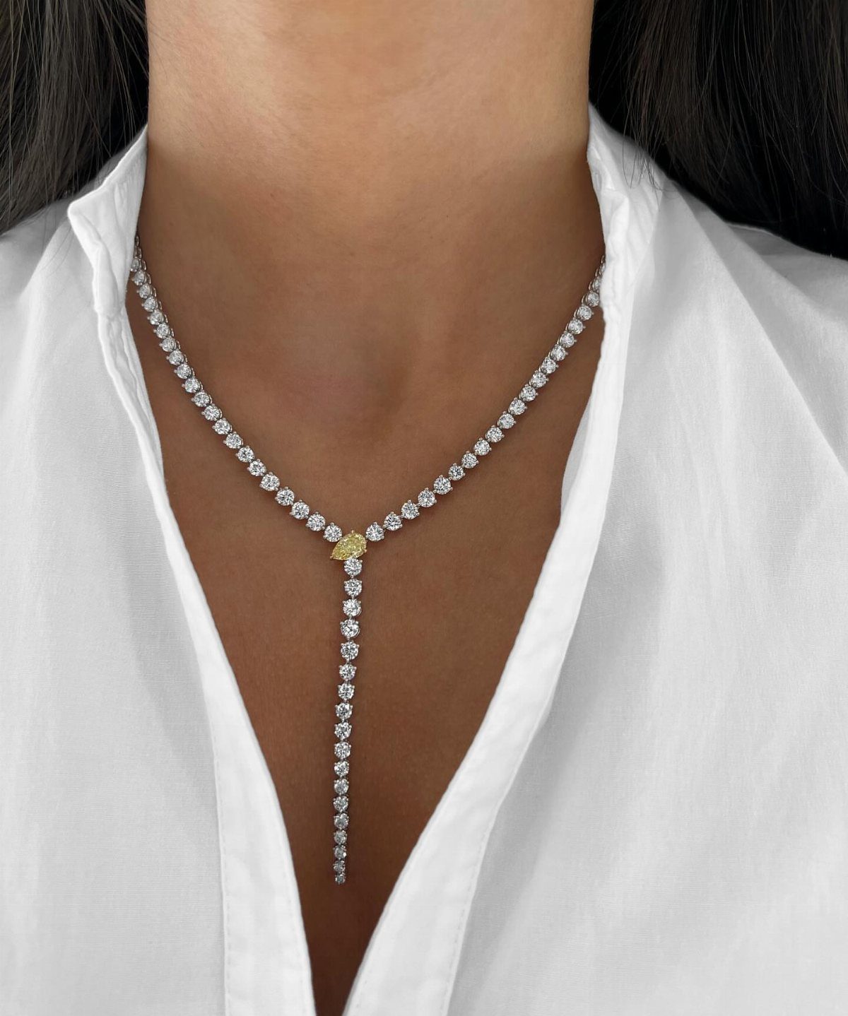 Diamond lariat necklace with a yellow center stone worn over a white shirt.