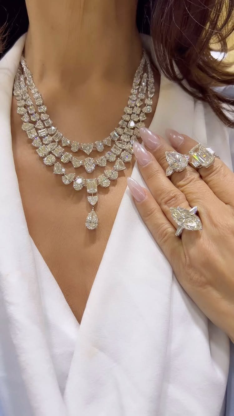 Multi-layered diamond necklace and large diamond rings worn by a person in white.
