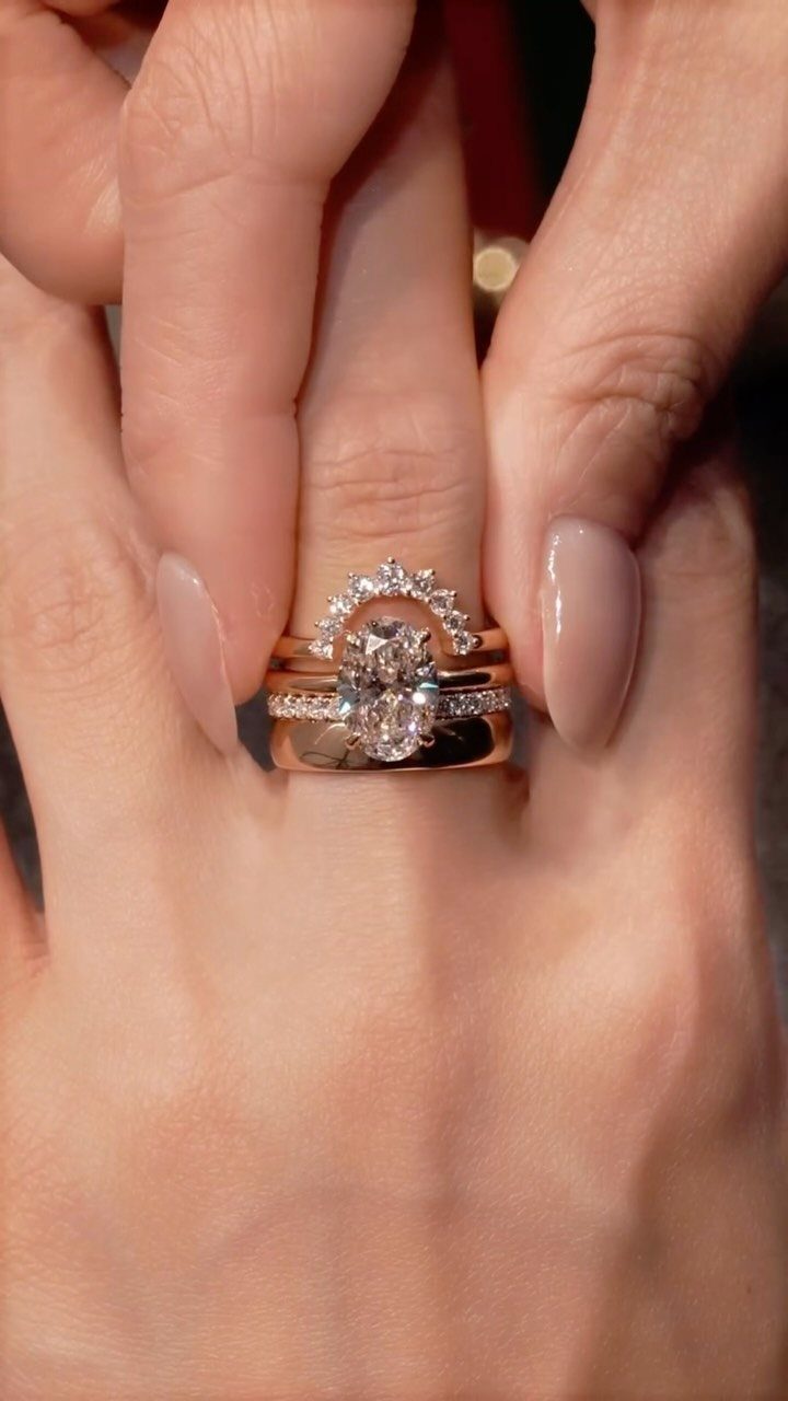 Rose gold diamond rings with an oval center stone on a woman's finger.