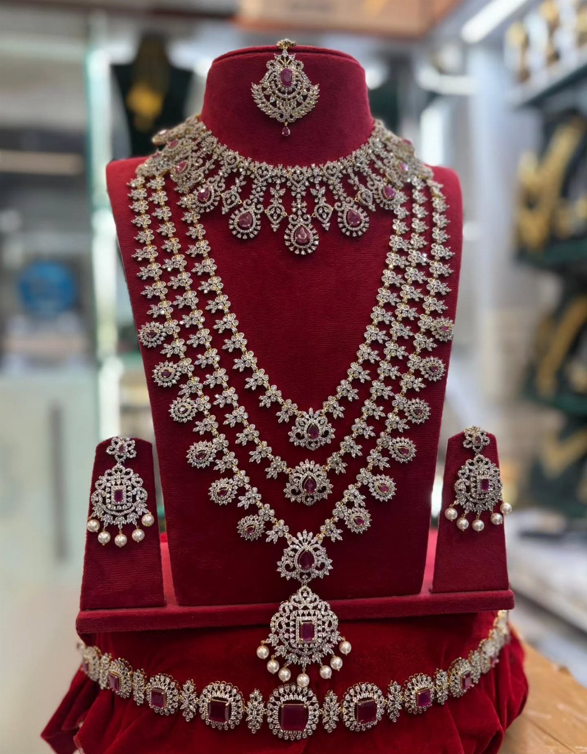 Ornate diamond and ruby bridal jewellery set displayed on a red velvet bust.