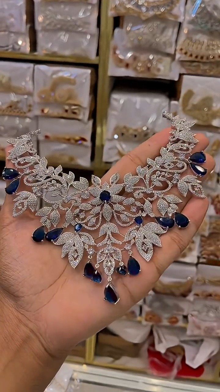Ornate silver diamond necklace with blue gemstones held in a person's hand.