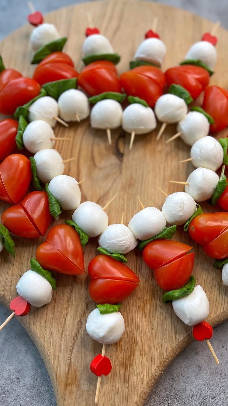 Heart-shaped cherry tomatoes, mozzarella balls, and basil leaves on wooden skewers.