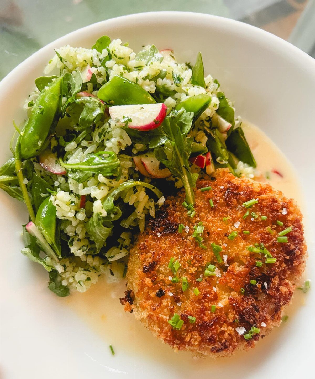 Golden-brown crab cake with chives served with a fresh green vegetable salad.