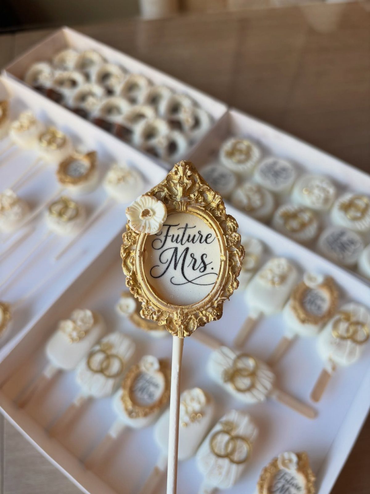 White chocolate cake pops with gold wedding rings and Future Mrs. frame topper.