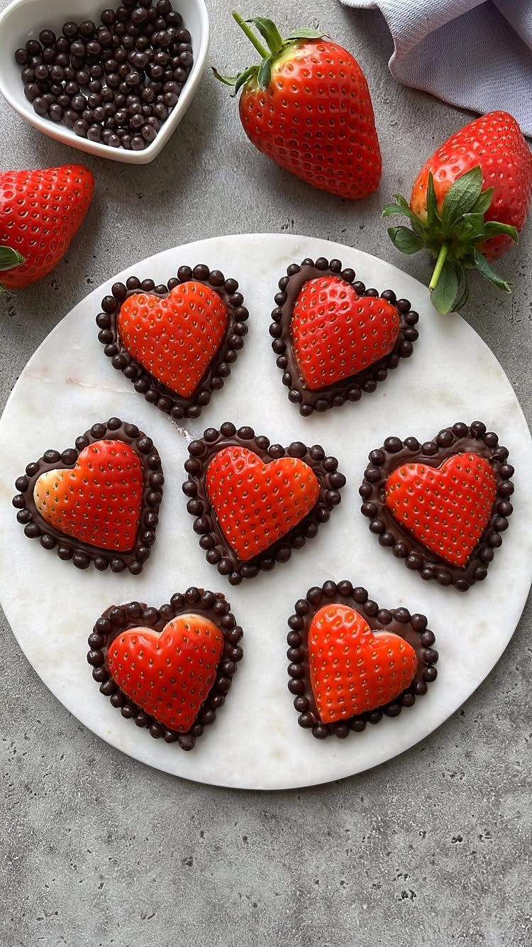 Heart-shaped chocolate-dipped strawberries on a white marble platter with fresh strawberries.