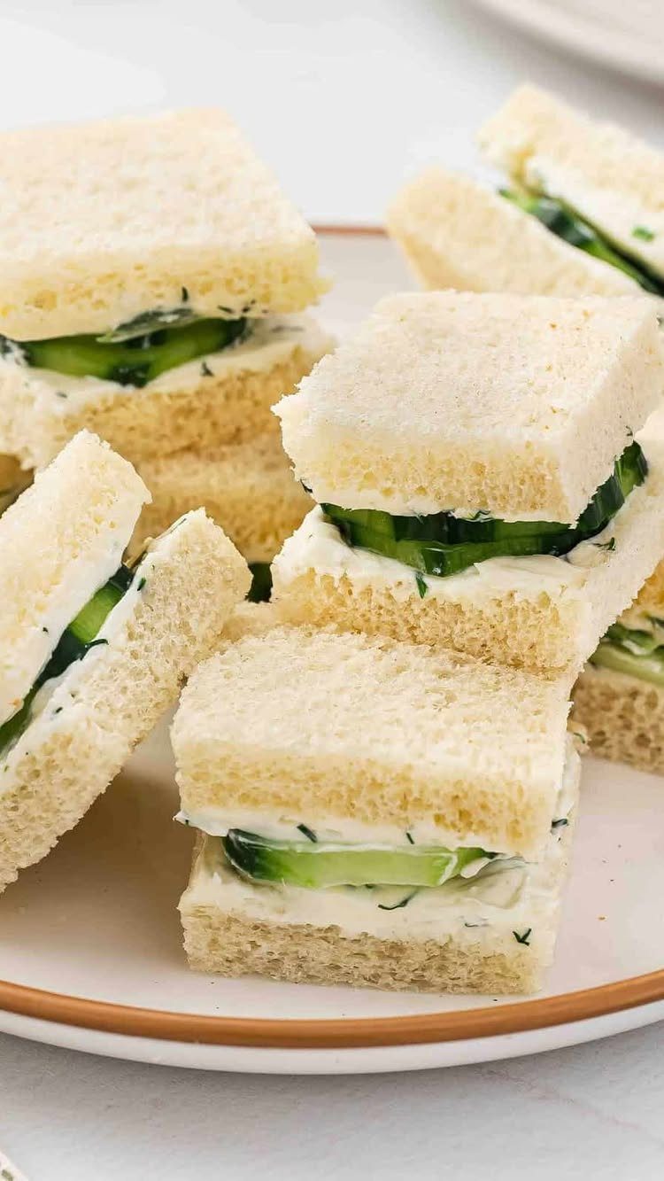 Cucumber tea sandwiches with cream cheese and herbs on a white plate.